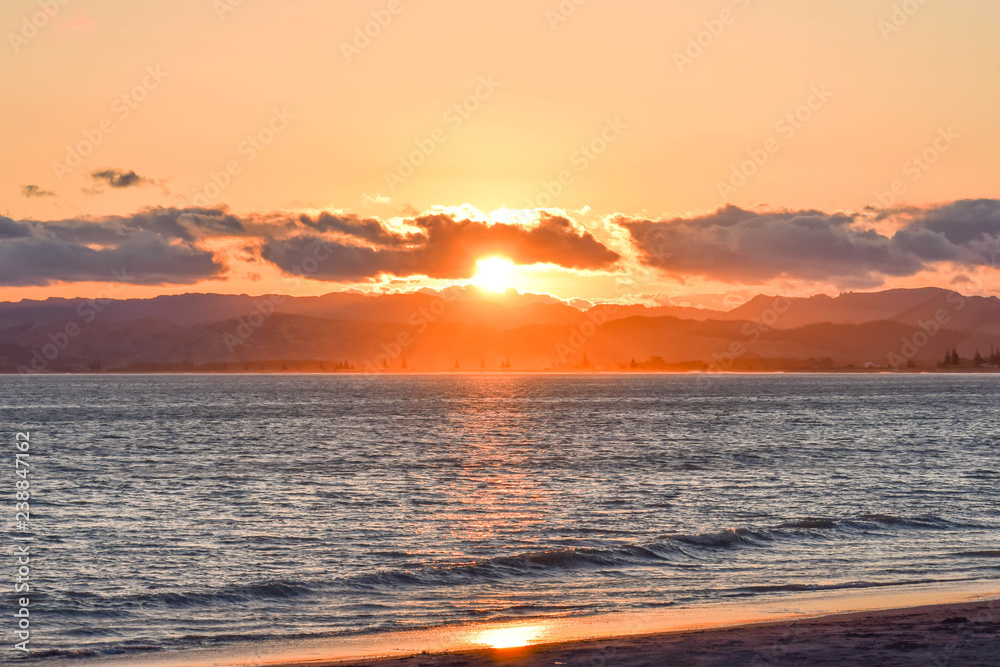 The bright sun sets in the distance above the coutryside of Gisborne, New Zealand.