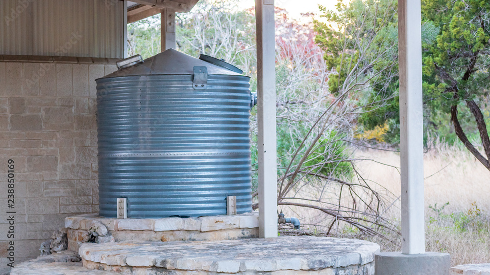 Corrugated steel water storage tank on top of flagstone masonry structure, with small stone fountain in front Corrugated steel water storage tank on top of flagstone masonry structure, with small stone fountain in front