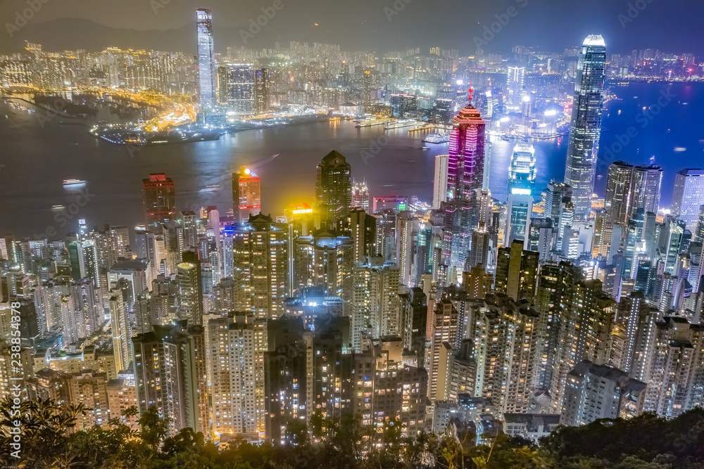 Hong Kong skyline at night as seen from Victoria Peak. Illuminated skyscrapers in foreground, Hong Kong harbor in background.