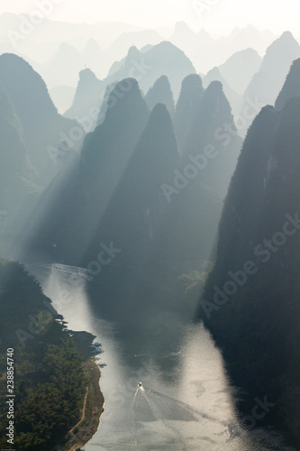 Karst Limestone hills in silhouette at sunrise over Li River as seen from Xianggong Mountain, near Guilin, China. Sun rays shining between hills.