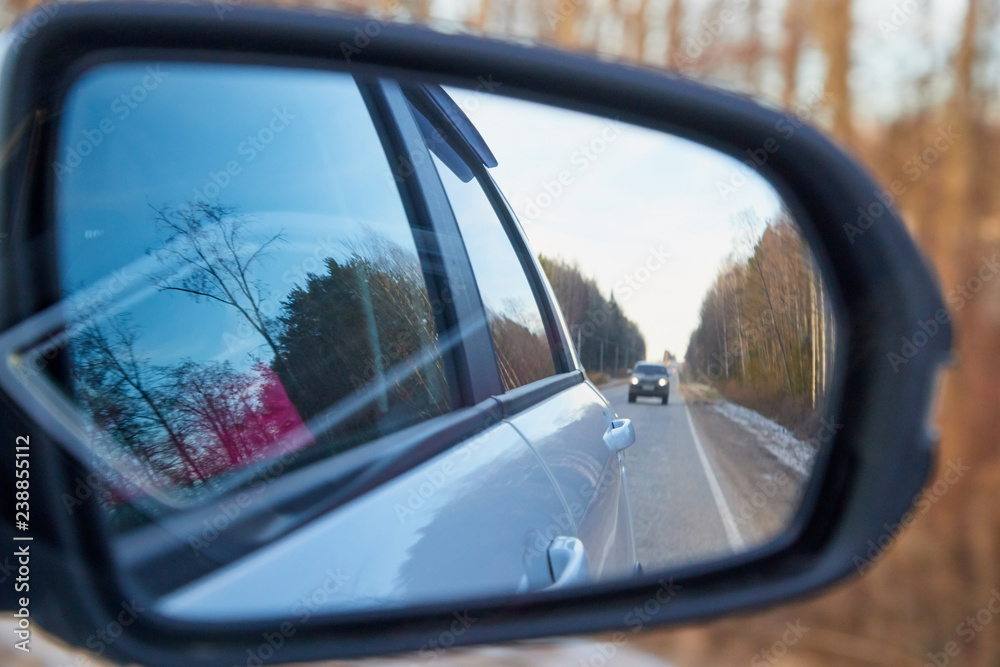 Side mirror of the car and the reflection of the road in it. Autumn landscape