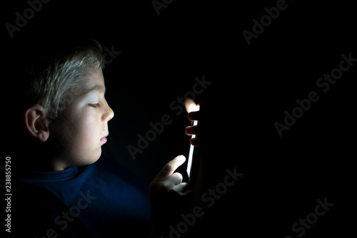 Young child using his mobile phone at night in the dark. Gaming or texting photo