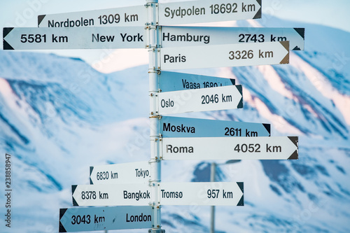 Big pole with directions signs and distances to cities of the world. Blue sky, mountains covered with snow. Longyearbyen, Spitsbergen, Norway photo