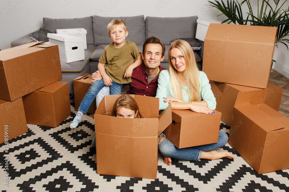 Picture of young couple with son and daughter sitting on floor among cardboard boxes Picture of young couple with son and daughter sitting on floor among cardboard boxes