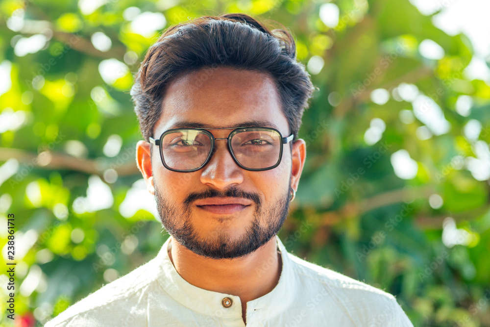 handsome and young indian male model beard and black hair haircut,fashion  earring and glasses on a background of green tropical  man  businessman student relaxing on the beach by the sea Stock