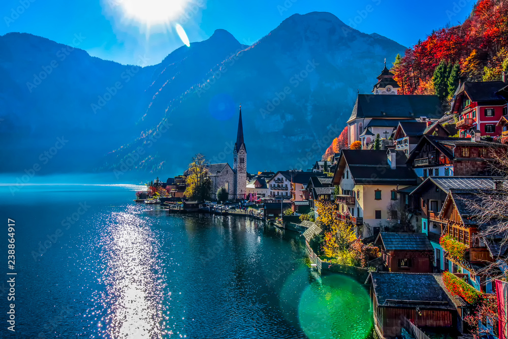 Beautiful picturesque view on Hallstatt old historic village and lake with blue sky, historic church and mountains with sunrays 