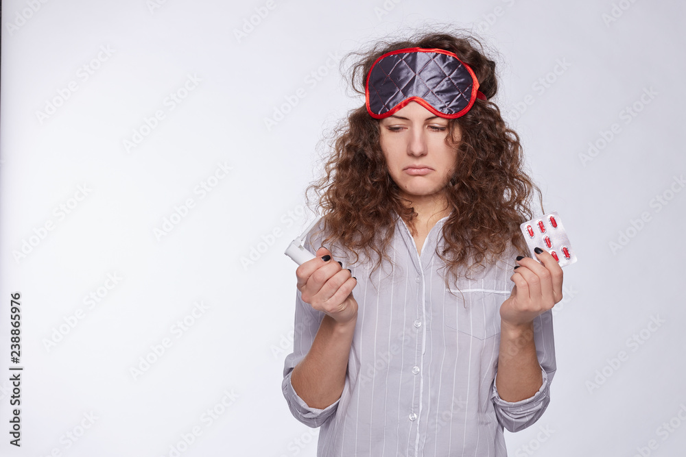 Negative human emotions and feelings. Indoor studio shot of unhappy young woman suffering from bad health or migraine after waking up on midday, having stressed painful look, holds medicine. Negative human emotions and feelings. Indoor studio shot of unhappy young woman suffering from bad health or migraine after waking up on midday, having stressed painful look, holds medicine.