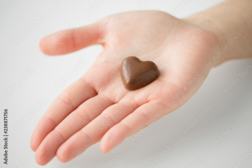 valentines day, sweets and confectionery concept - close up of hand holding heart shaped chocolate candy valentines day, sweets and confectionery concept - close up of hand holding heart shaped chocolate candy