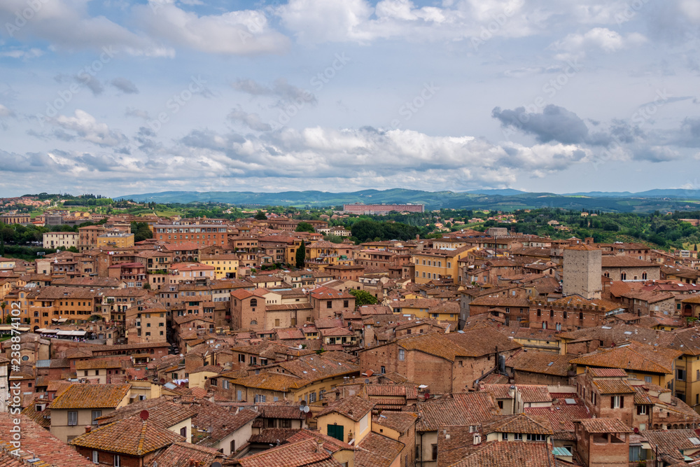 Cityscape of Siena (Tuscany) Italy with lots of houses an a wide view over the tuscan countryside and a cloudy sky