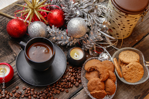 Black cup of coffee, cookies filled with chocolate, Christmas balls, candles and coffee beans. Close-up on the old rustic wooden table