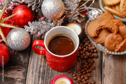 Big red cup of coffee, cookies filled with chocolate, Christmas balls, candles and coffee beans. Close-up on the old rustic wooden table