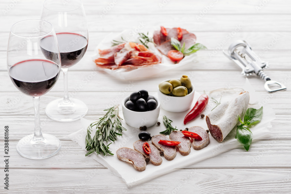 close up view of tasty meat appetizers and glasses of red wine on white wooden surface close up view of tasty meat appetizers and glasses of red wine on white wooden surface