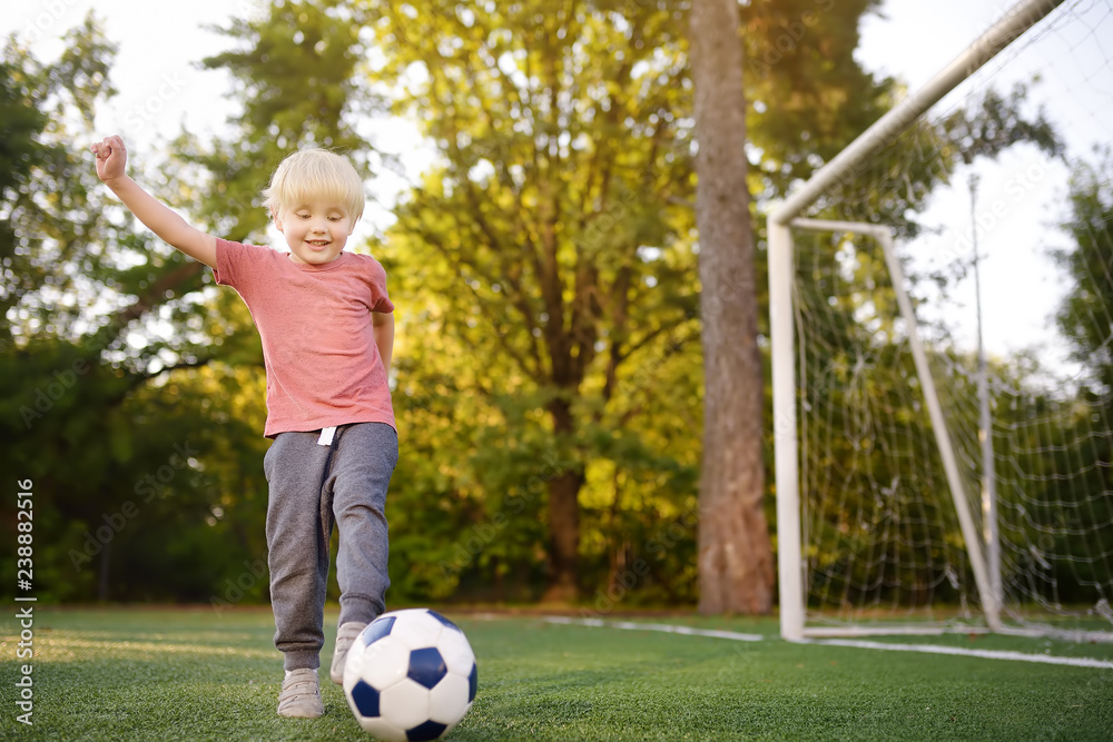 Little boy having fun playing a soccer/football game on summer day. Active outdoors game/sport for children. Little boy having fun playing a soccer/football game on summer day. Active outdoors game/sport for children.