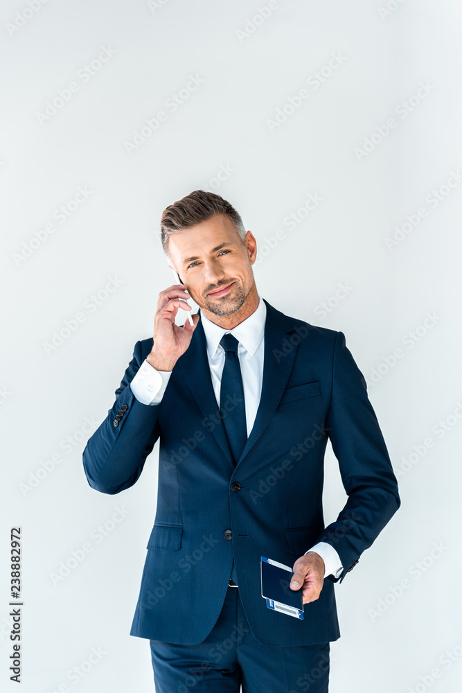 cheerful handsome businessman talking by smartphone and looking at camera isolated on white