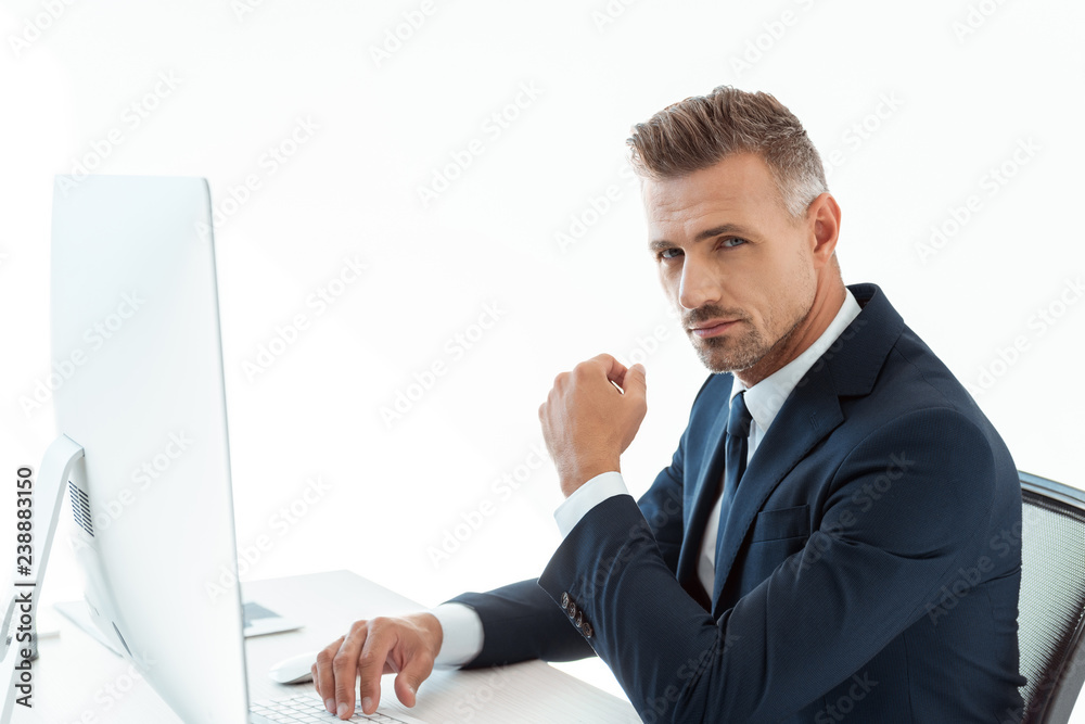 handsome businessman sitting at table with computer and looking at camera isolated on white handsome businessman sitting at table with computer and looking at camera isolated on white