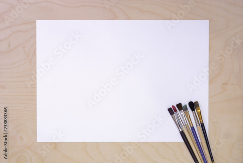 Artist Paint Brushes with Blank White Paper Lying on Wooden Table. Drawing Tools in Art Studio. Top View.