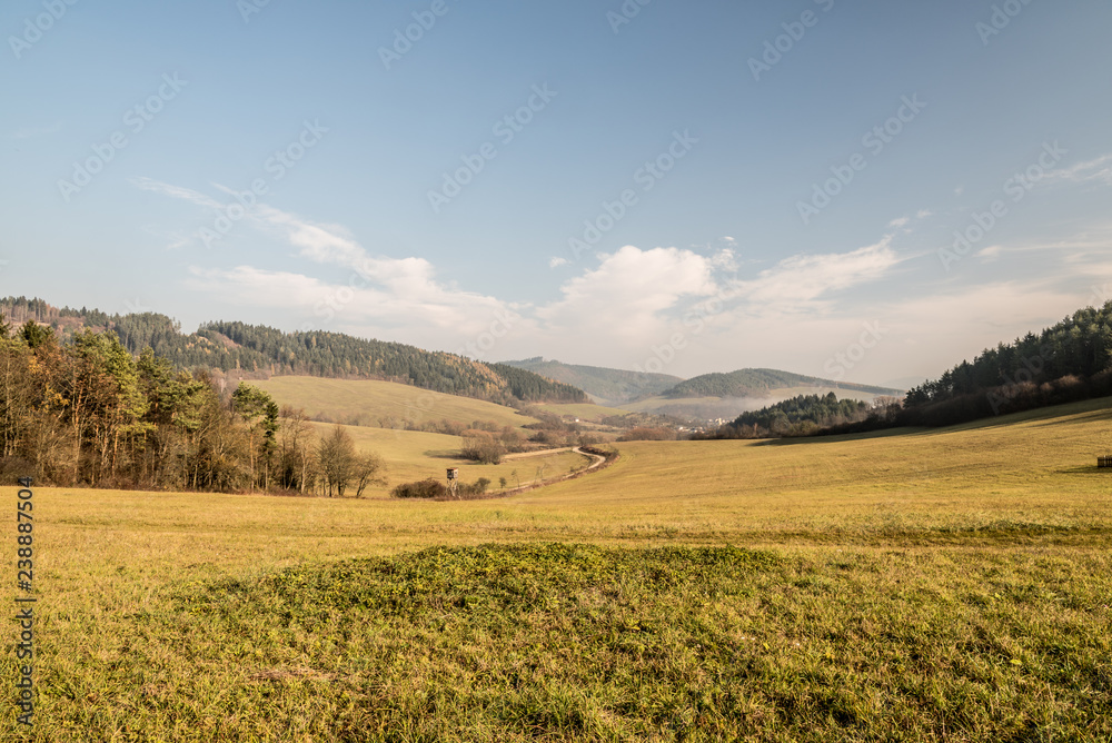 beautiful autumn scenery with meadows, smalleer hills, dirt road and blue sky with clouds