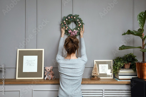 Obraz na plátně Girl hanging a wreath on a gray wall, sun light