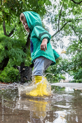little boy is jumping in a puddle in rubber boots in rainy weather