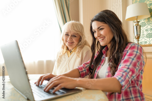 Woman types on the laptop while sitting with her senior mother.