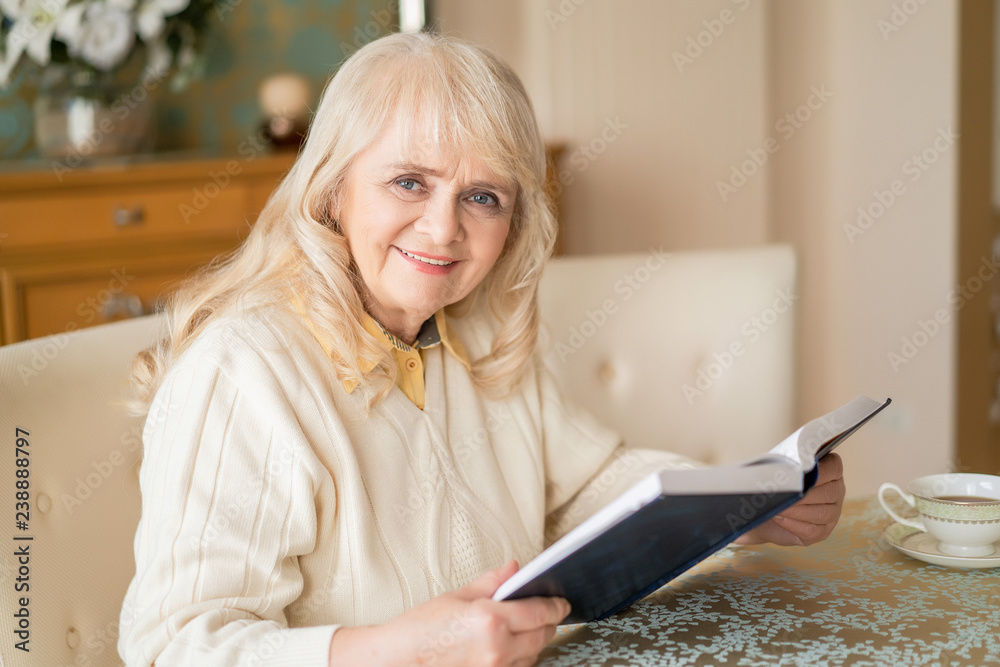 Elegant senior woman reads book at table and having tea Elegant senior woman reads book at table and having tea