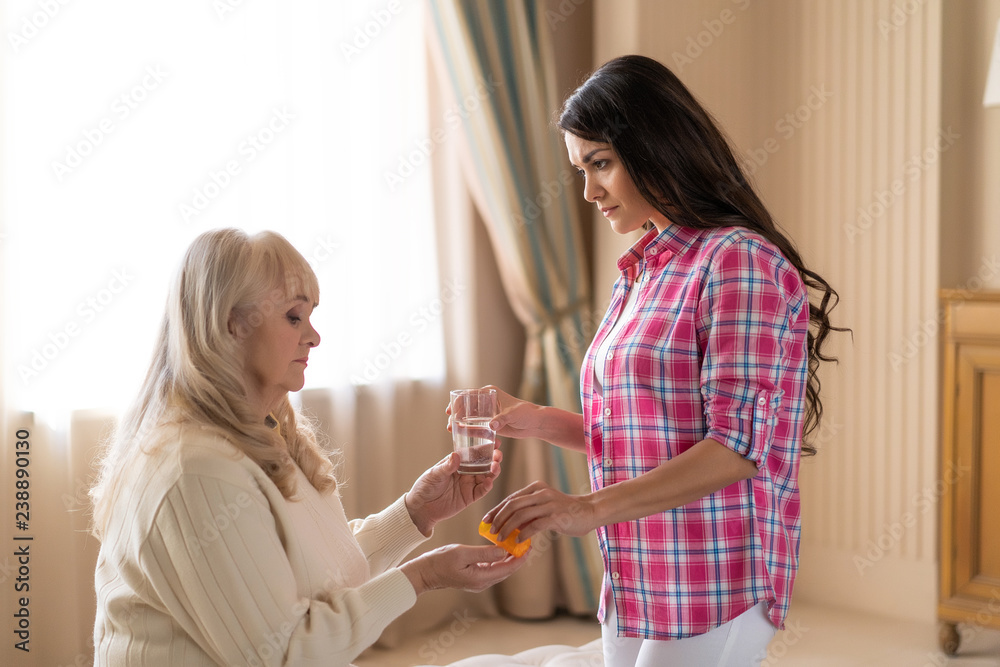 Daughter gives her senior mother pills and water Daughter gives her senior mother pills and water