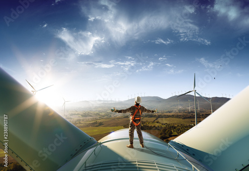Happy engineer feel success after good work. He standing a top of windmill and looking beautiful sunset