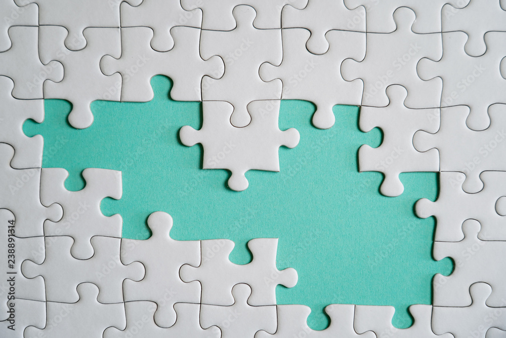 Fragment of a folded white jigsaw puzzle and a pile of uncombed puzzle elements against the background of a colored surface. Fragment of a folded white jigsaw puzzle and a pile of uncombed puzzle elements against the background of a colored surface.