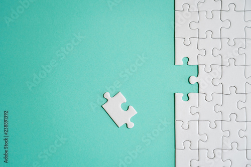 Fragment of a folded white jigsaw puzzle and a pile of uncombed puzzle elements against the background of a colored surface.