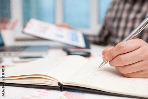 Businessman writes in a notebook while sitting at a desk.