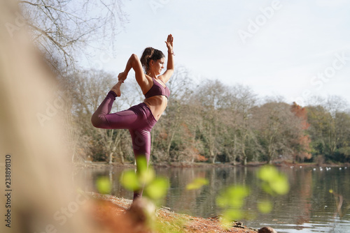 Stunning brunette practicing yoga outdoors by lake in fall