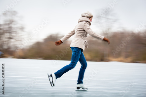 Foto Young woman ice skating outdoors on a pond on a freezing winter day