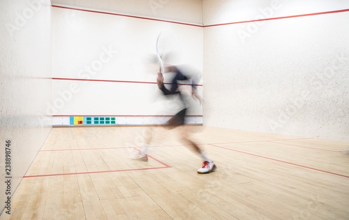 Squash player in action on a squash court (motion blurred image; color toned image)