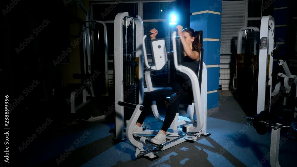 The girl is working on the chest muscles on the simulator. Exercise is the reduction of hands sitting on the simulator (butterfly). The girl is working on the chest muscles on the simulator. Exercise is the reduction of hands sitting on the simulator (butterfly).