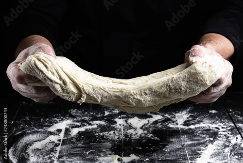 cook stretches kneaded dough from white wheat flour photo