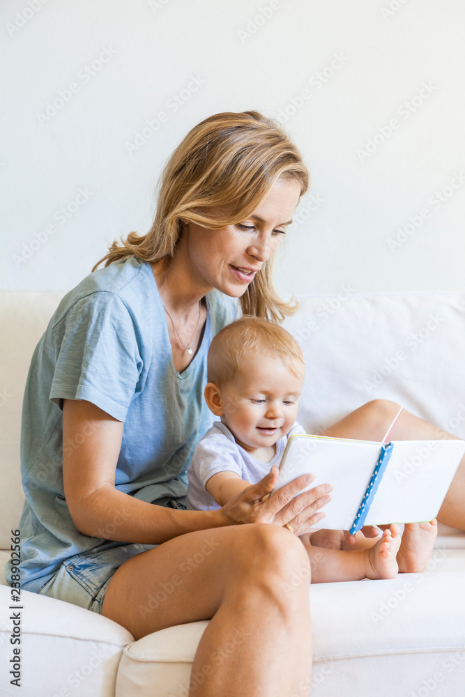 Mother and baby girl sitting on couch looking at picture book Mother and baby girl sitting on couch looking at picture book