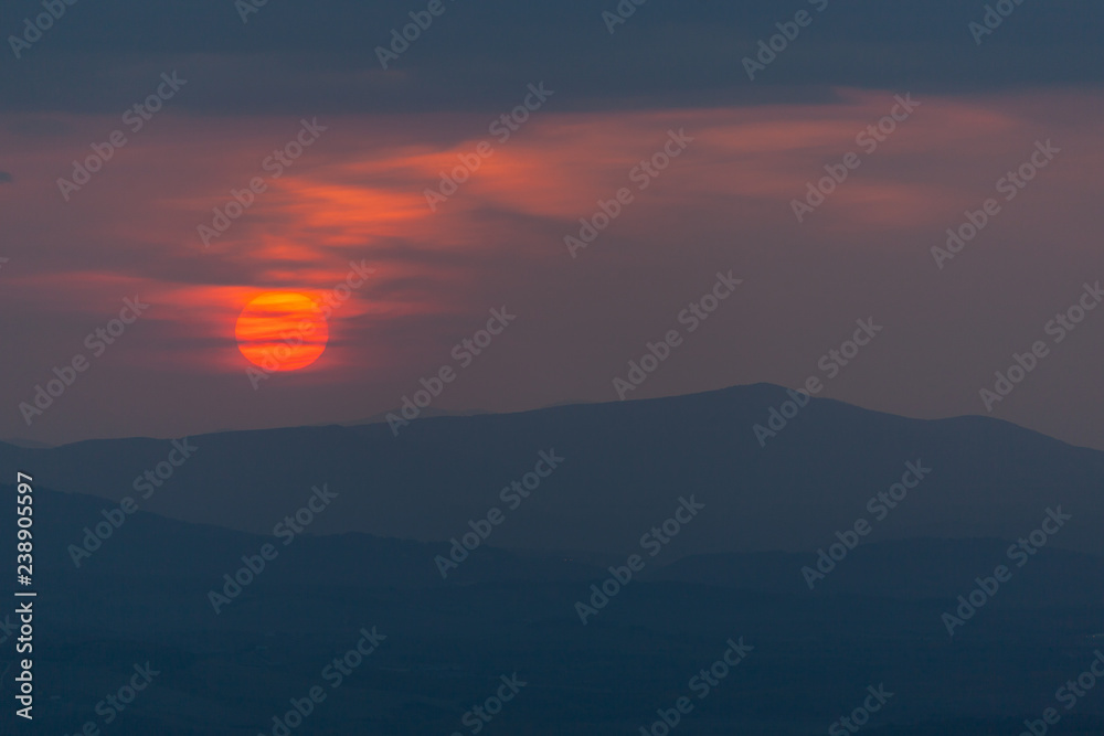 Mystic sunset in the Tuscany region with red solar disk and silhouettes of the hills, Italy