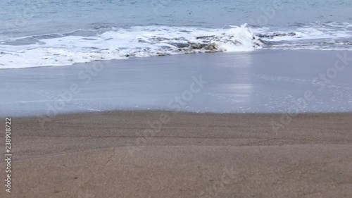 Soft and delicate waves flowing on smooth sandy coast.