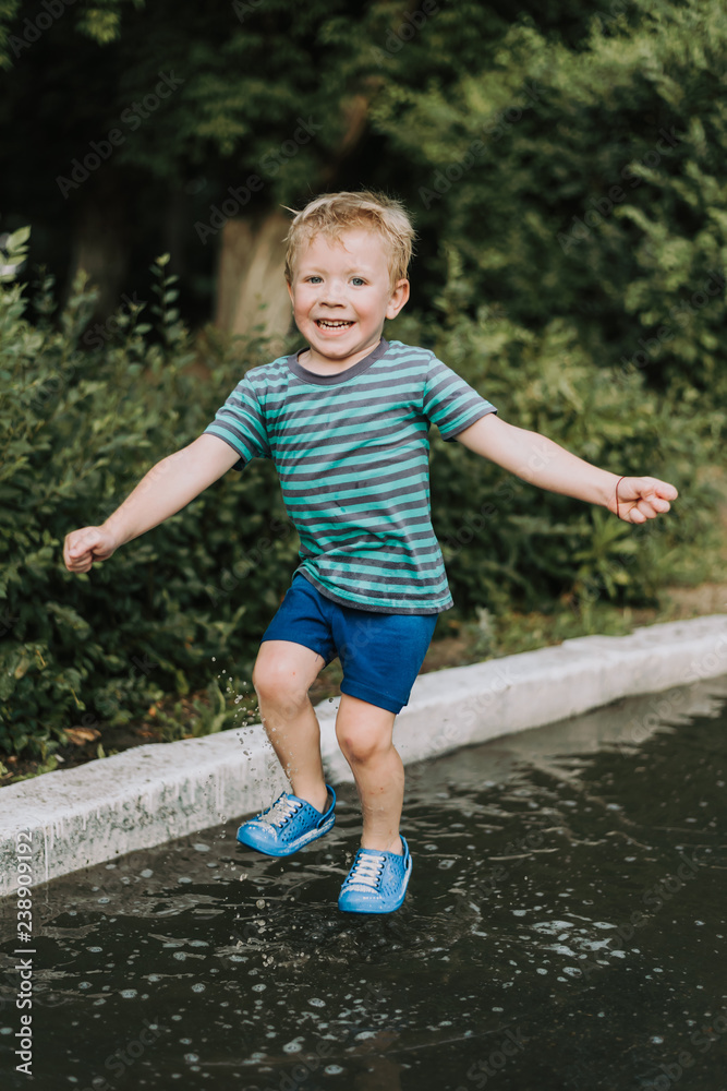 little boy jumping in a puddle in summer