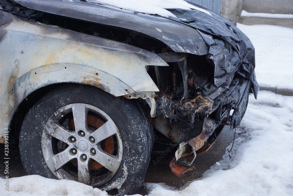 part of a black car burnt into a crash with a bumper and a wheel in the snow on the street part of a black car burnt into a crash with a bumper and a wheel in the snow on the street