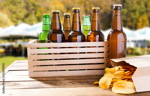 Fototapeta Naklejka Na Ścianę i Meble -  many bottles of beer and pack of chips on wooden table on blurred summer background