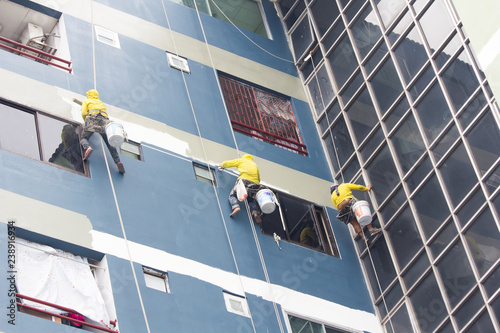 painters hanging on roll, painting color on building wall.