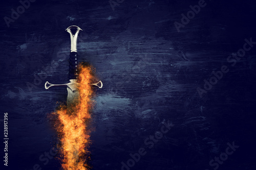 low key image of silver sword in the flames of fire. fantasy medieval period.