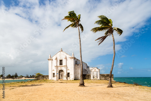 Church and fortress of San Antonio on Mozambique island, with two palm trees on sand. Indian ocean coast, Nampula province, Mozambique. Fortim de Santo António na Ilha de Moçambique. 
