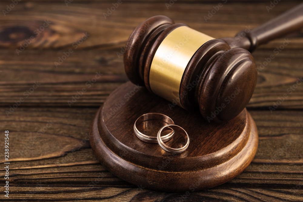 a pair of gold engagement rings, a judge's hammer on a wooden table background. family law, divorce and conflict.
