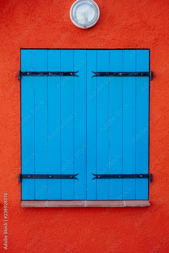 Blue wooden closed shutters on window against orange wall Blue wooden closed shutters on window against orange wall