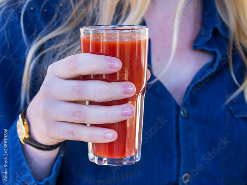 A glass with tomato juice is held by a blond woman.