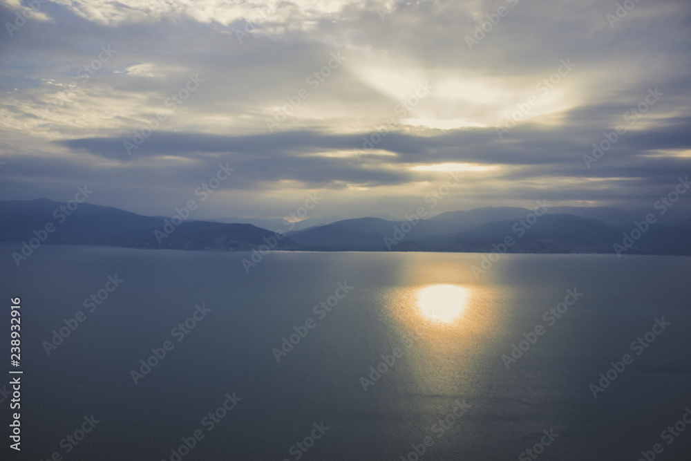 abstract soft focus nature landscape with calm sea water and mountain horizon background in morning sun rise time and foggy cloudy weather
