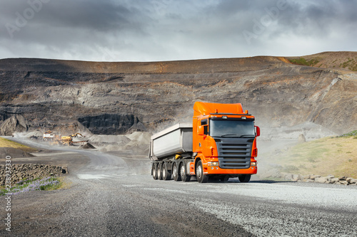 Modern orange european truck with white heavy duty dump trailer drives after load from quarry in a sunny day photo