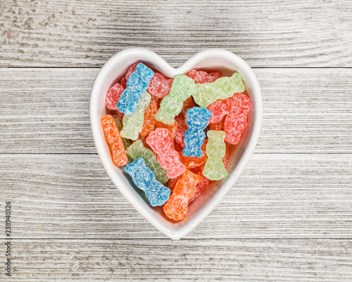 Variety of different color sweet and sour candy or sugar junk food in a heart shaped bowl.